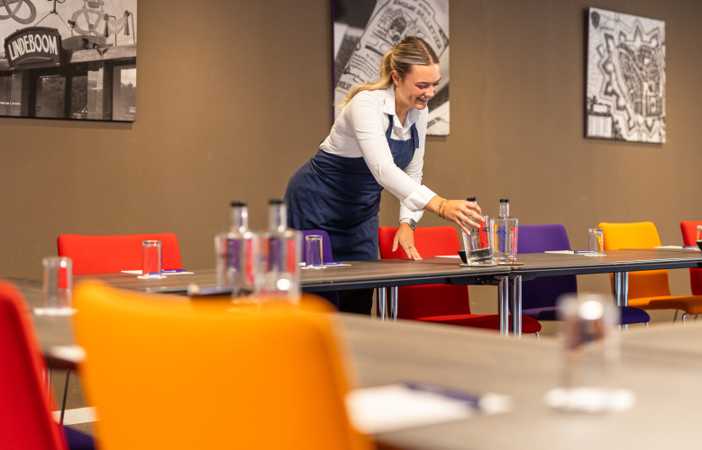 Foto van gastvrouw in vergaderzaal die water klaarzet