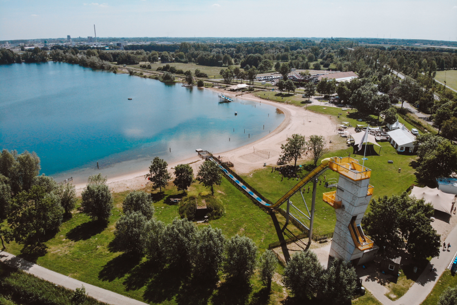 Overzicht van het terrein met water, hoge glijbaan, strand en het hoofdgebouw.