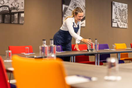 Foto van gastvrouw in vergaderzaal die water klaarzet