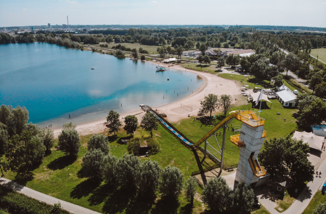 Overzicht van het terrein met water, hoge glijbaan, strand en het hoofdgebouw.