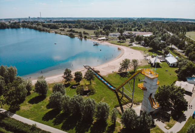 Overzicht van het terrein met water, hoge glijbaan, strand en het hoofdgebouw.